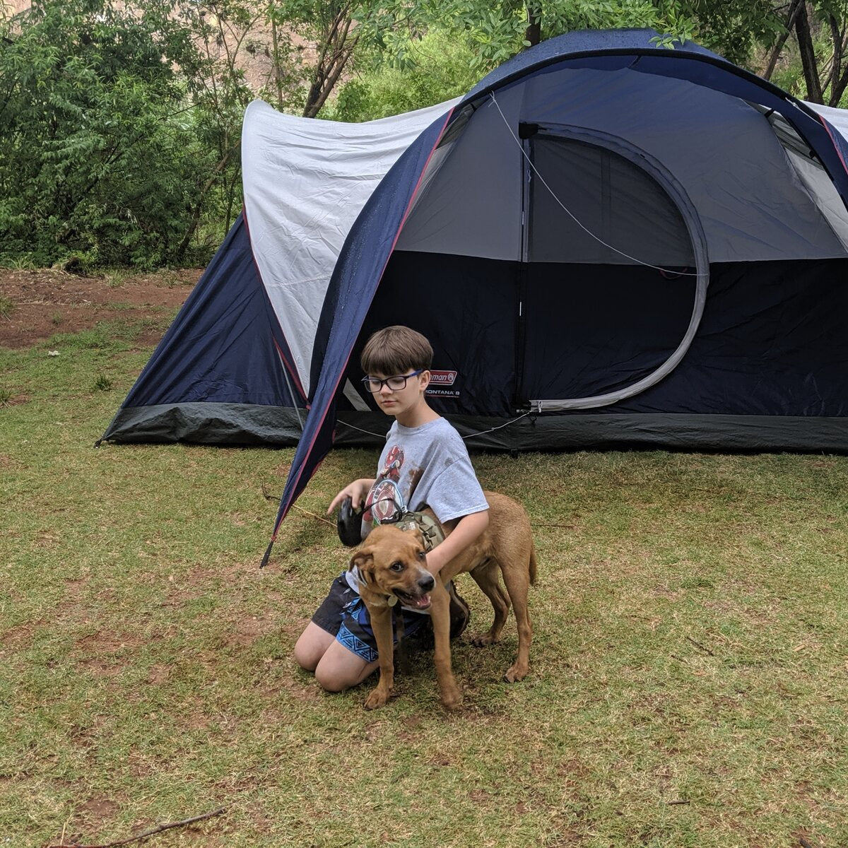 Brian's son kneeling with their rescue dog Sarge in front of a tent in the Arizona mountains